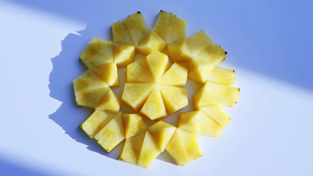 Top view shows pineapple slices arranged into floral circle on smooth white surface, bathed in warm sunlight with soft shadows, vivid yellow color, crisp texture, minimal styling, centered