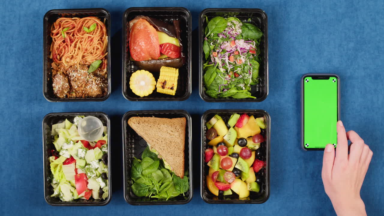 Top View of Healthy Meal Prep Containers and Hand Using Green Screen Smartphone