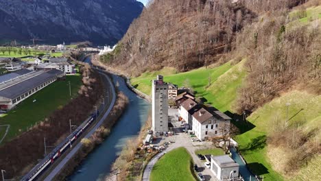 aerial approaching shot of tower and rolling mill factory beside river and riding train