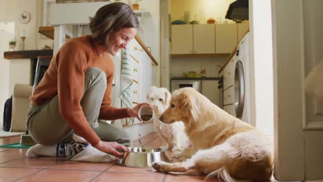 smiling caucasian woman feeding her pet dogs pouring food into bowl in kitchen at home