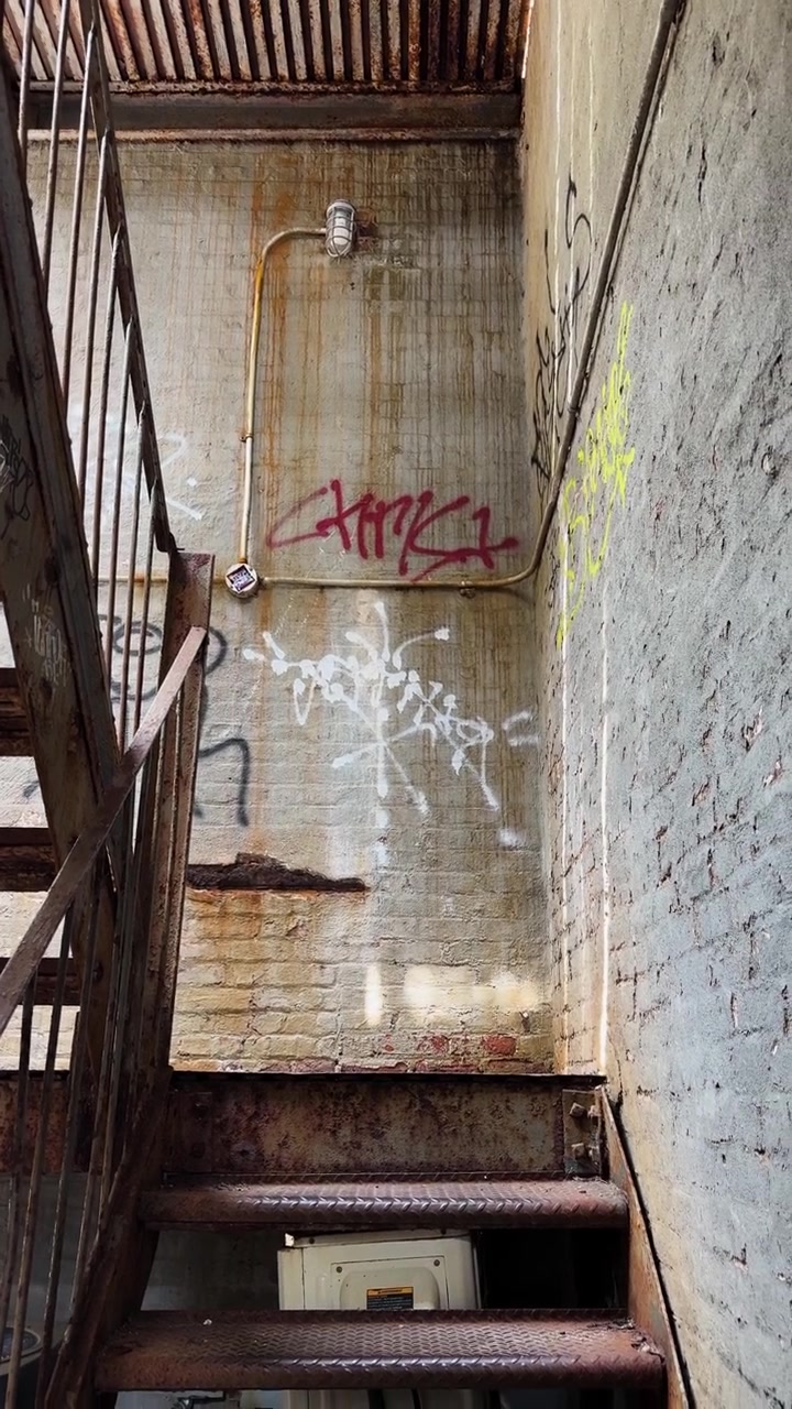 Rusty metal stairs in gritty urban alleyway with tagged brick walls and grime