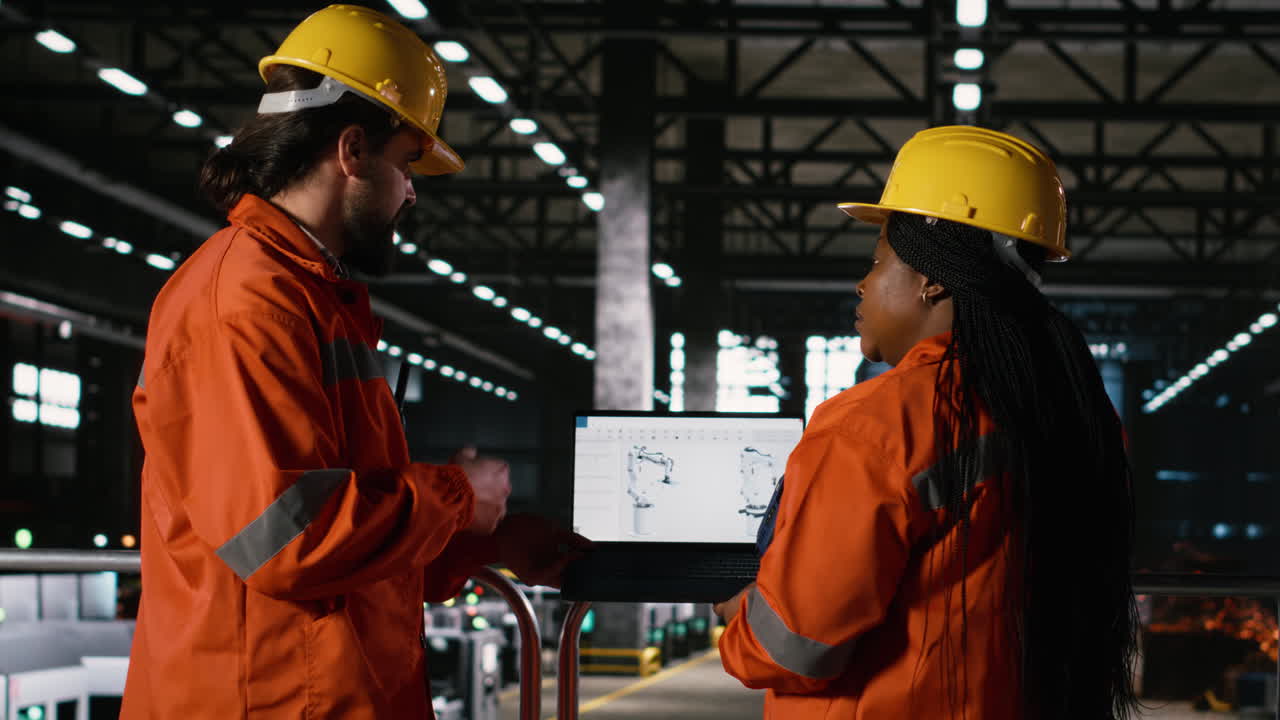 Professional team reviews robot arm software on laptop in heavy industry factory