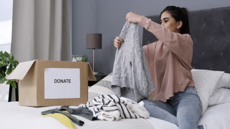 una mujer empacando ropa en una caja de donaciones en casa