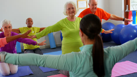 Rear-view-of-female-trainer-training-senior-people-in-exercise-at-fitness-studio-4k