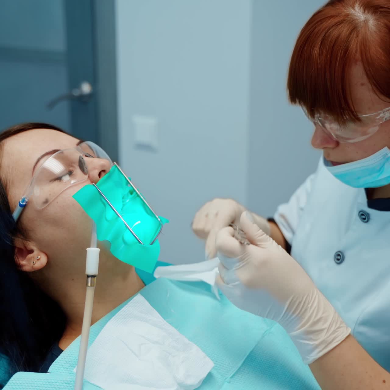 Woman patient with toothache during tooth treatment. Professional female dentist in mask and glasses treating teeth using medical instruments at stomatology clinic.
