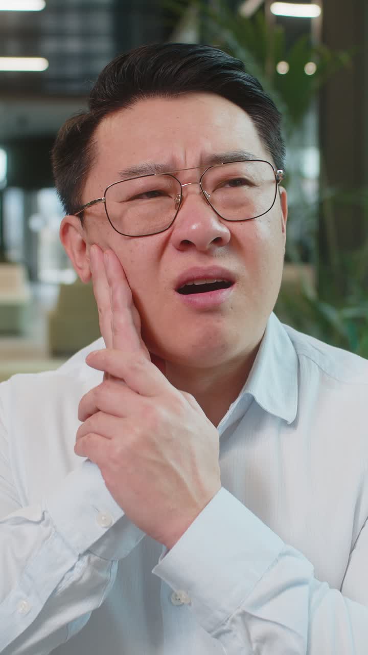 Chinese businessman in office lobby working on laptop and feeling toothache in modern office lobby