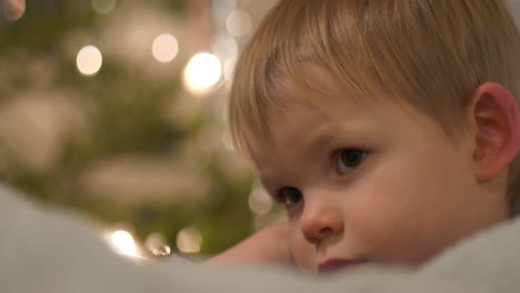 tired toddler during christmas, christmas tree background, close up