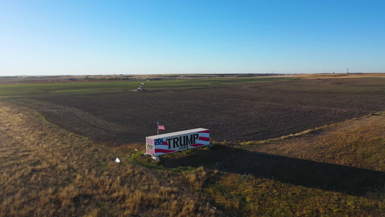 video de drones aéreos vote por donald trump 2024 cartel de la campaña electoral presidencial pintado en un gran camión o remolque en tierras agrícolas rurales con plataforma petrolera y hierba alta en medio de la nada