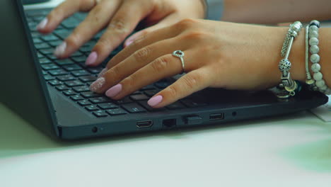 woman's hand with pink polished nails, typing fast on laptop keyboard