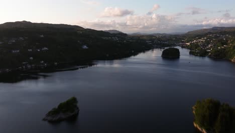 Aerial-hyperlapse-above-lake-inlet-or-fjord-in-Norway-surrounded-by-homes-hidden-in-lush-trees