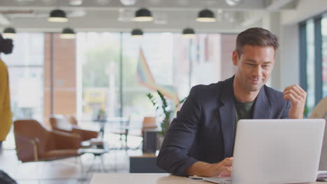 Businessman-And-Businesswoman-Having-Informal-Meeting-By-Desk-In-Modern-Open-Plan-Office