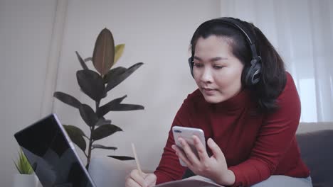 Asian-woman-on-redshirt-using-a-tablet-with-headphone-for-meeting-online-at-home