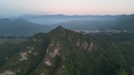 Drone-view-in-Guatemala-flying-in-front-of-a-green-mountain-surrounded-by-volcanos-on-a-cloudy-day-in-Atitlan