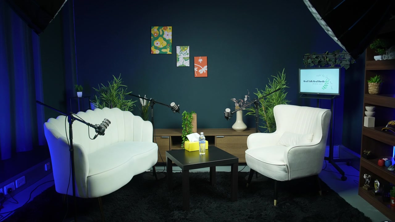 Allestimento di uno studio podcast professionale vuoto con microfoni, poltrone bianche e decorazioni interne moderne. Parete di sfondo blu scuro, concetto di registrazione di trasmissioni mediatiche e palco per interviste.