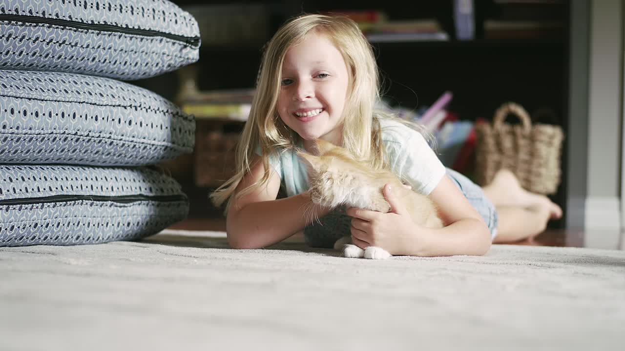 A little girl laying on the floor and petting a kitten and smiling