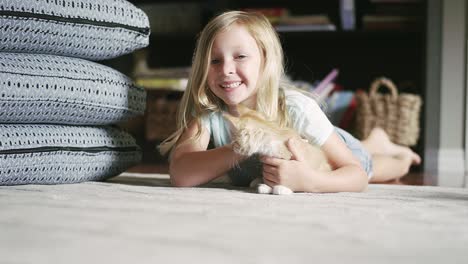 a little girl laying on the floor and petting a kitten and smiling