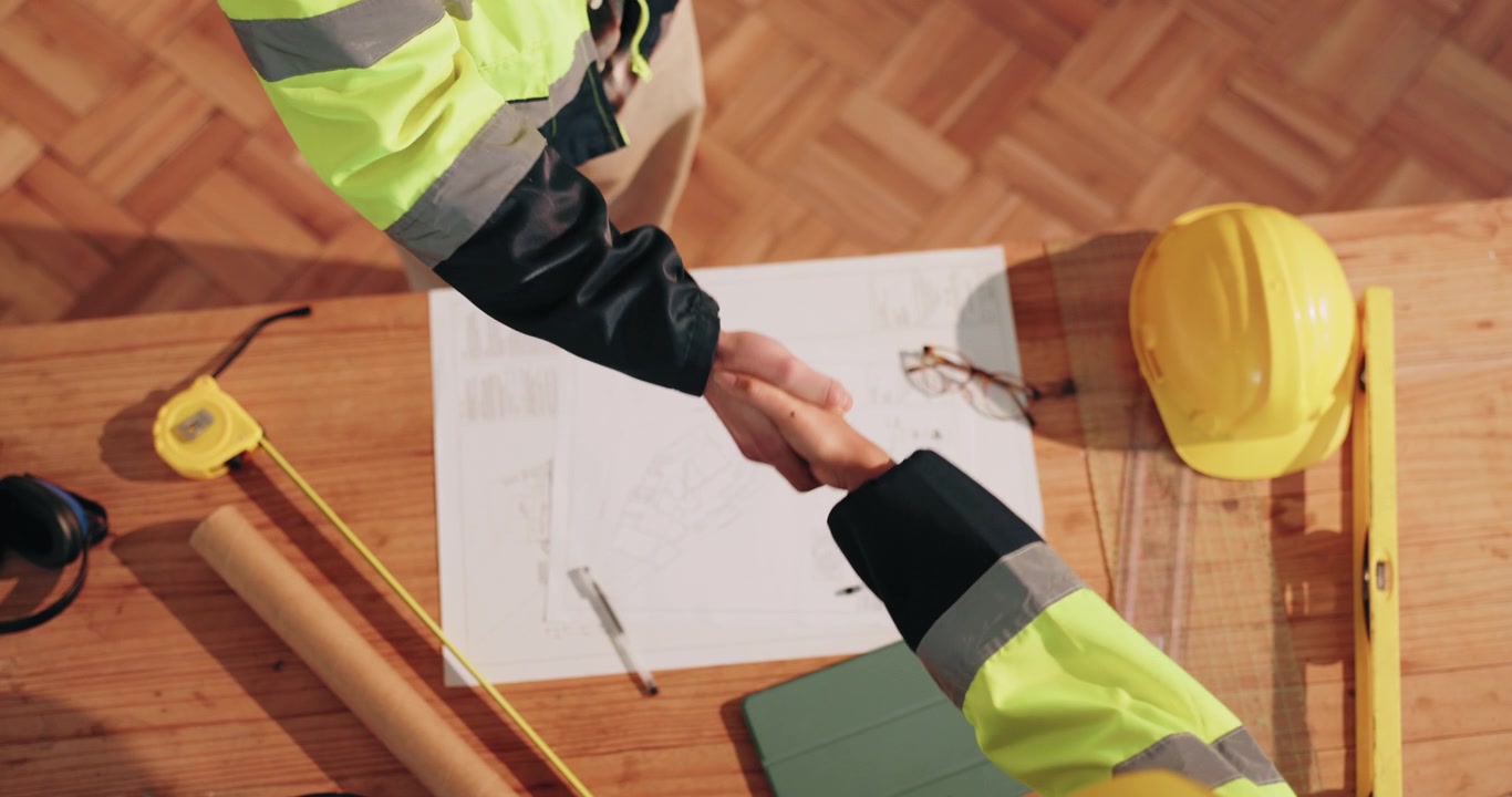 Construction Engineers Shaking Hands Over Blueprints in Office
