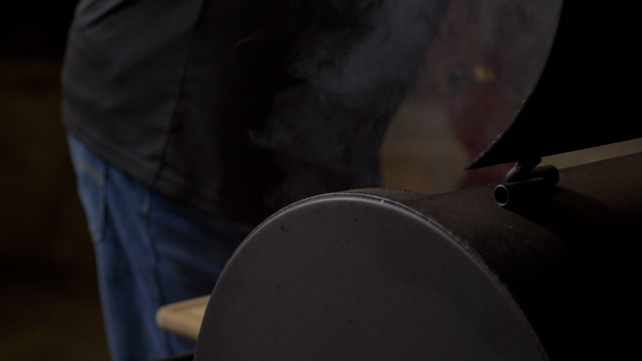 el hombre usa pinzas para mover la salchicha en el fumo de la barbacoa