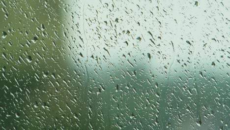 Rain-drops-sliding-slow-on-window-glass-in-rainy-day,-medium-closeup-shot