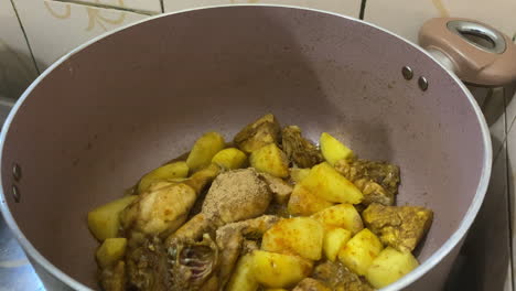 especias vertidas sobre patatas y trozos de pollo chisporroteantes en una olla