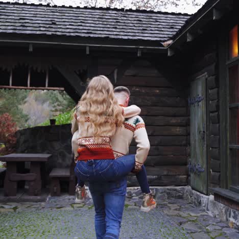 love story. dating outside. young ?ouple on wooden house in forest background. guy carries girl on his back