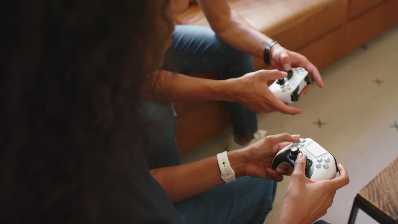 Two players are pressing start and adjusting thumbs on white controllers while playing on low couch