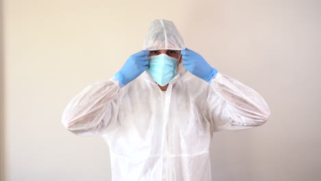 doctor in ppe suit putting on hood while looking directly into the video camera