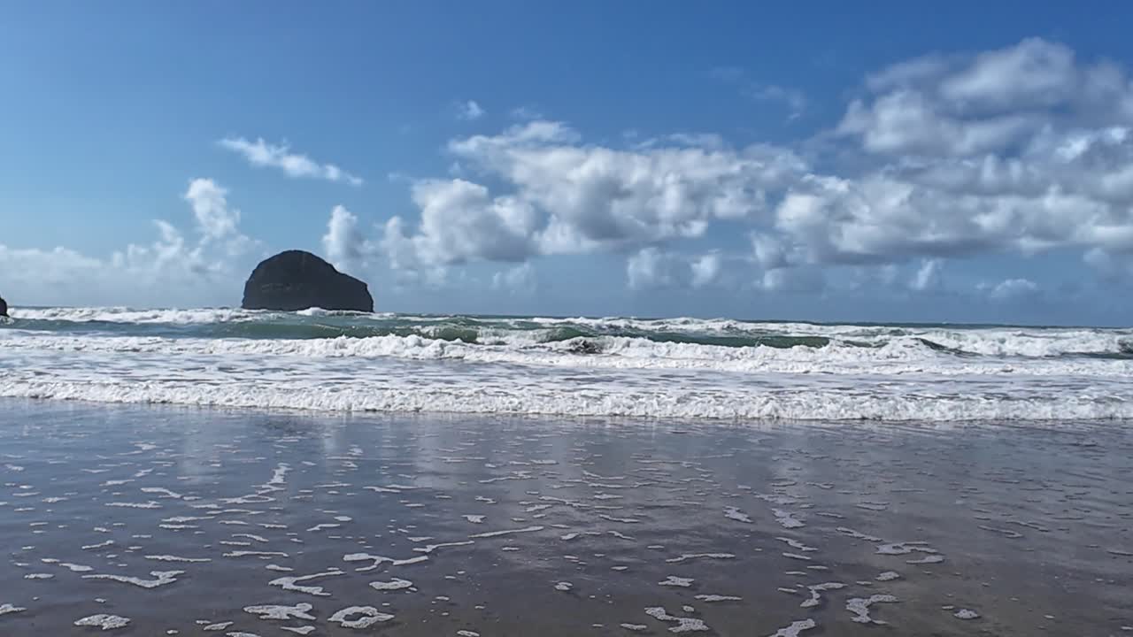 Drone shot capturing the scenic beauty of Trebarwith Strand Beach, Cornwall. Majestic waves crash against the shore under a vast blue sky, creating a tranquil yet dynamic seascape