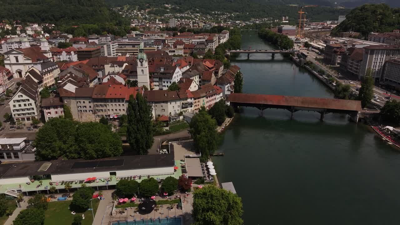 Reverse drone shot revealing Olten old town, clock tower, and wooden bridge over the Aare river in Switzerland