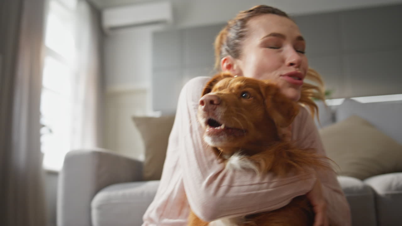 Woman hugging adorable dog with happy smile at home close up. Girl caressing pet