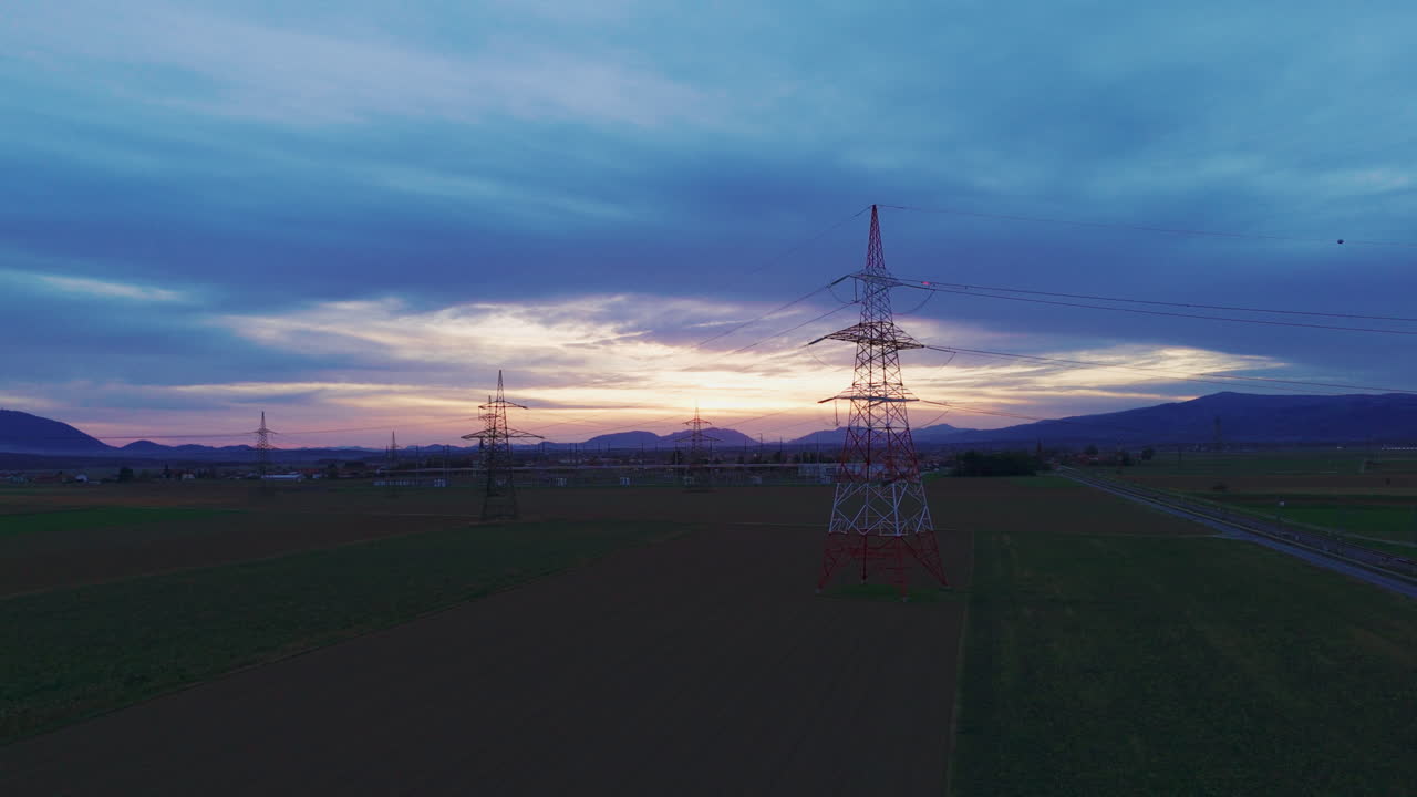 High voltage power lines and towers stand in a rural area during sunset the sky shows colors from