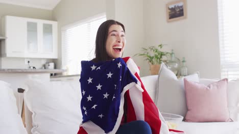 Happy-caucasian-woman-sitting-on-couch-with-flag-of-usa-and-watching-tv-in-living-room