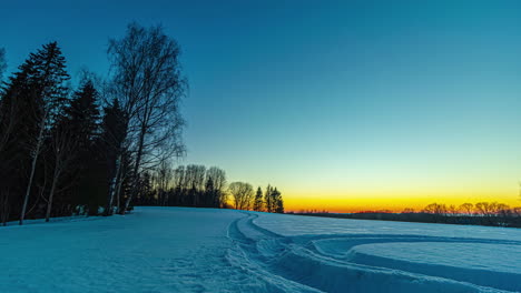 Goldener-Sonnenuntergang-Hinter-Einem-Schneefeld-Mit-Reifenspuren-Darin---Zeitraffer