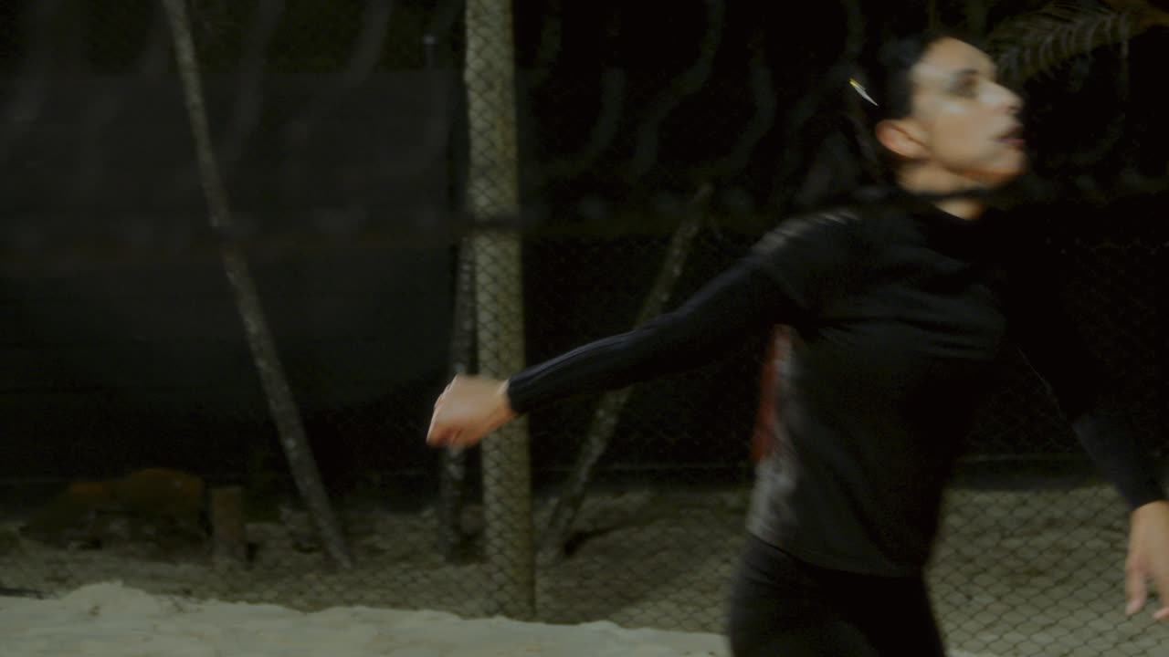 A woman plays volleyball on a sand court at night