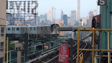 incoming seven train at queensboro plaza subway station with the silvercup studios and the manhattan skyline in the background, filmed in the early morning hours of a sunny day in new york city