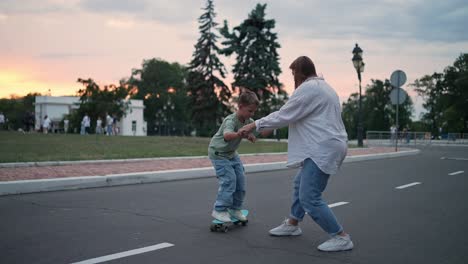 mother teaching son to skateboard at sunset