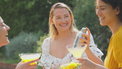 three female friends sitting outdoors in summer garden at home mixing cocktails