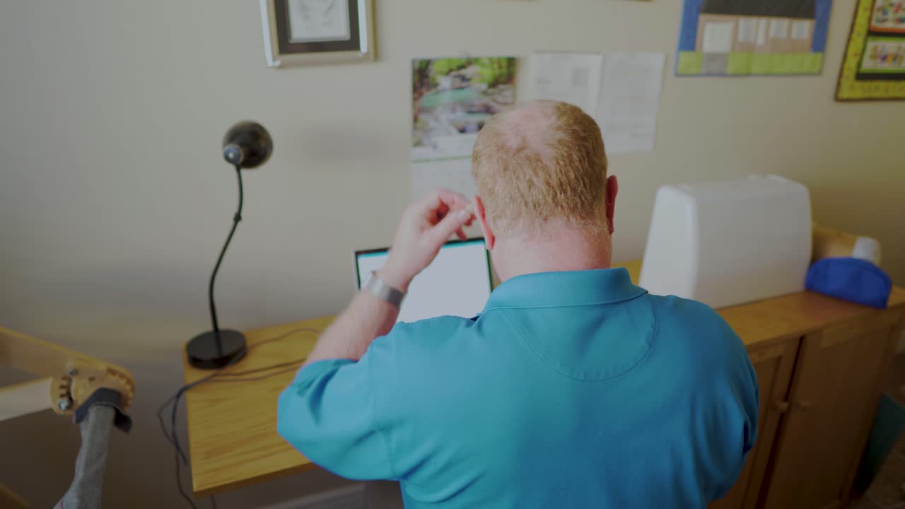 한 노인이 노트북 작업을 하기 전에 보청기를 착용합니다.