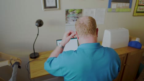 A-senior-man-puts-on-his-hearing-aids-before-working-on-his-laptop