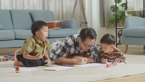 full body of asian father and sons lying on the floor in the room with plastic toy brick. drawing, talking, playing together at home, another son looking at his father then screaming, saying wow