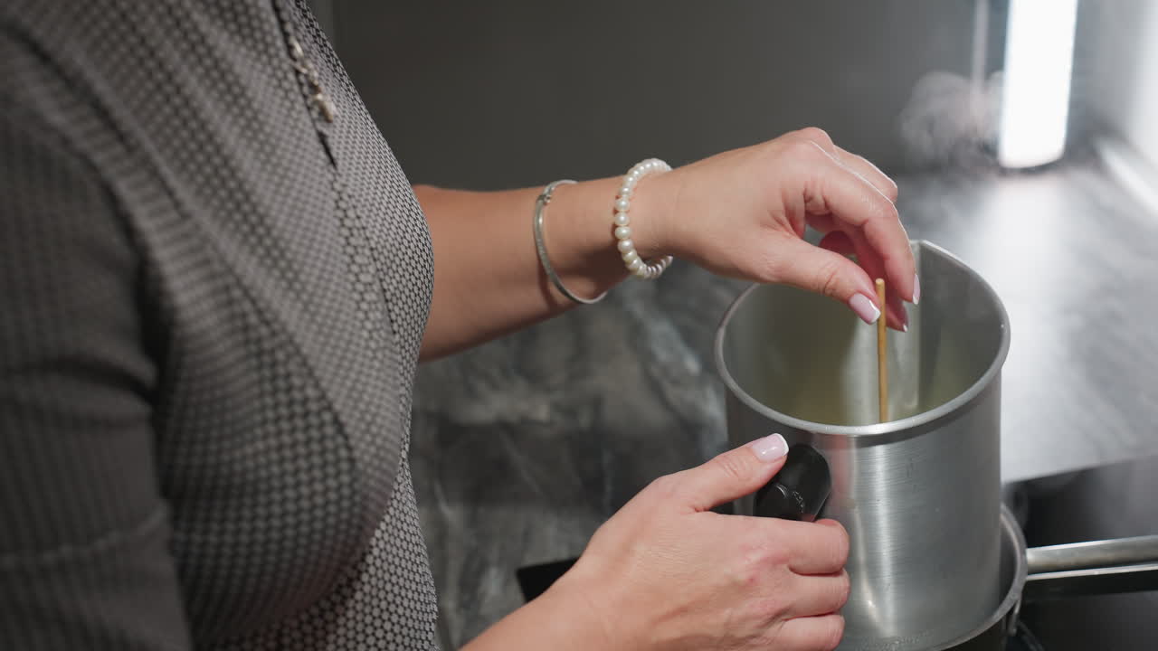 Grandma stirs mixture in metal container placed over pot of boiling water using left hand adorned with white beads and silver bracelet, showing traditional care, warmth, and hands-on cooking