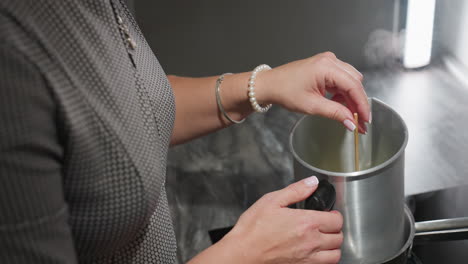 grandma stirs mixture in metal container placed over pot of boiling water using left hand adorned with white beads and silver bracelet, showing traditional care, warmth, and hands-on cooking