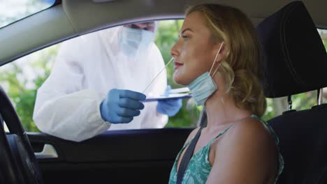 mujer caucásica sentada en el coche, con máscara facial, con una prueba de covid hecha por un trabajador médico al aire libre