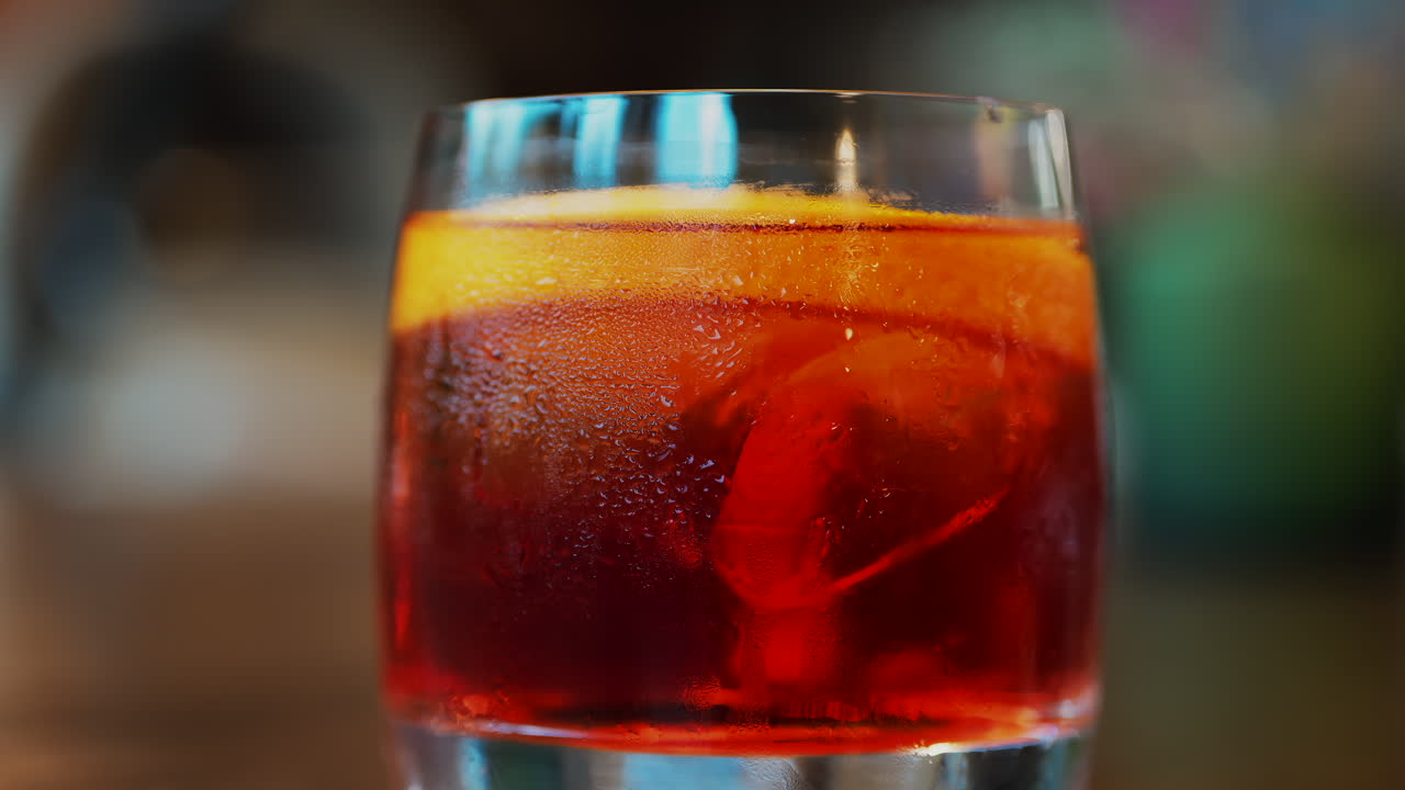 Close up of a Negroni cocktail with orange slice and ice cubes on a wooden table
