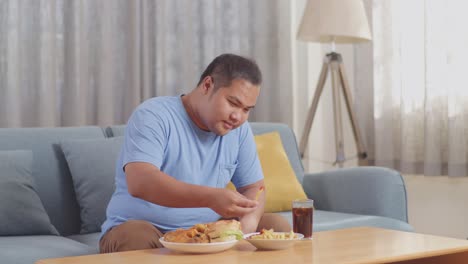 a fat asian man having french fries with ketchup then drinking a glass of coca cola while eating fast food on a sofa in the living room at home