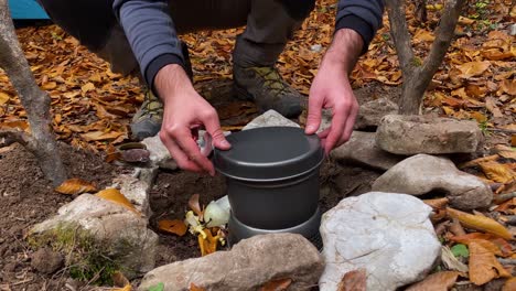 a traveler man cook food on stove vegetable mix hot meal in the bone fire place wild barbeque beside tent in the forest park stone pieces placed around and ground covered by orange autumn tree leave