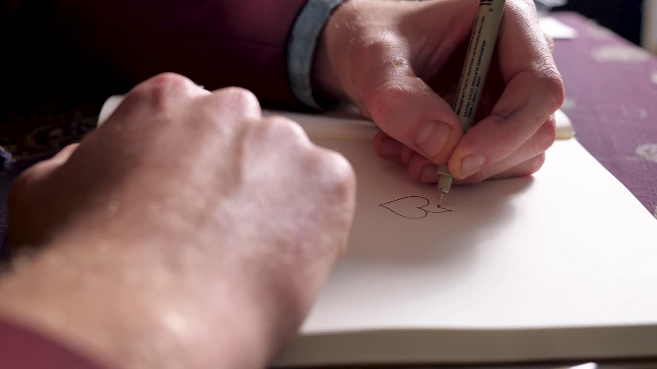 Young illustrator graphic designer drawing a heart with a fineliner in his sketchbook - close up - 4k
