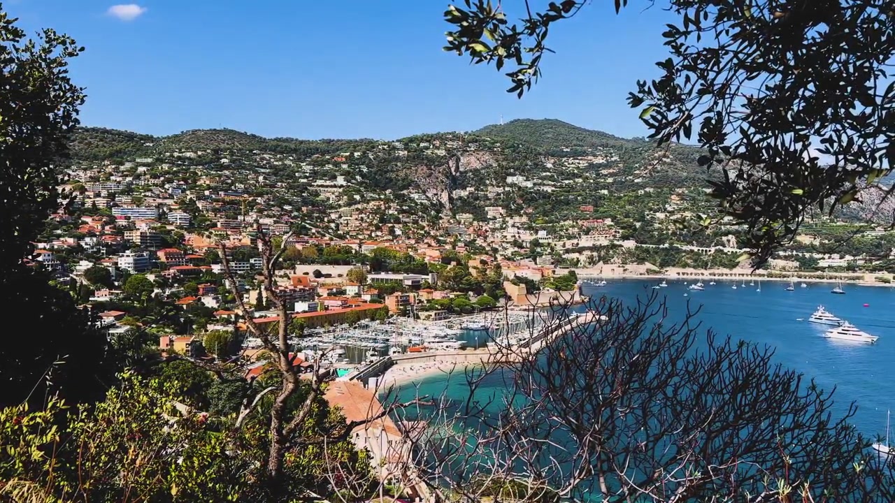 Vista elevata del porto turistico di Villefranche-sur-Mer, baia turchese, case sulla collina e yacht di lusso, naturalmente incorniciata dalla vegetazione mediterranea