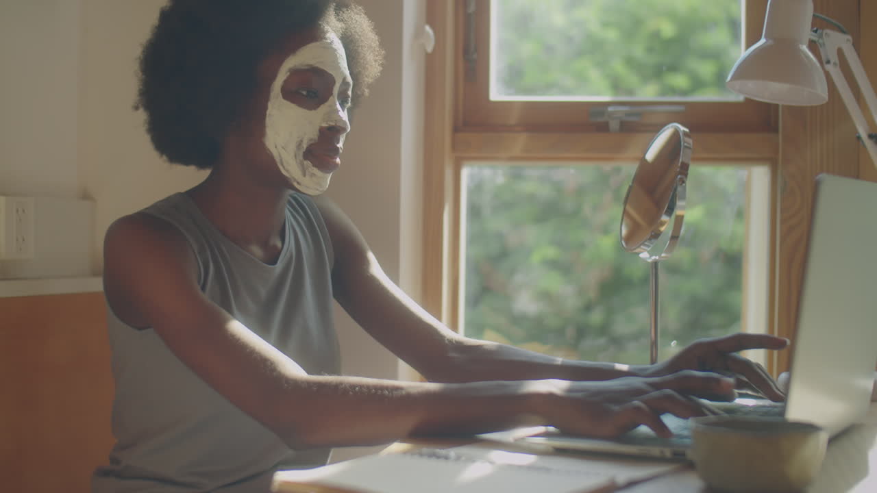 Black Woman with Facial Mask Working on Laptop at Home