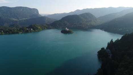 aerial drone fly above blue natural calm lake bled church of the mother of god, pristine atmosphere in slovenia, tiny island